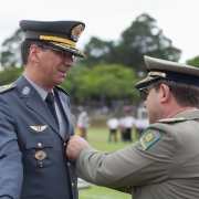 Cel Nivaldo Restivo recebe medalha em seu peito de outro oficial, observado por outro companheiro.