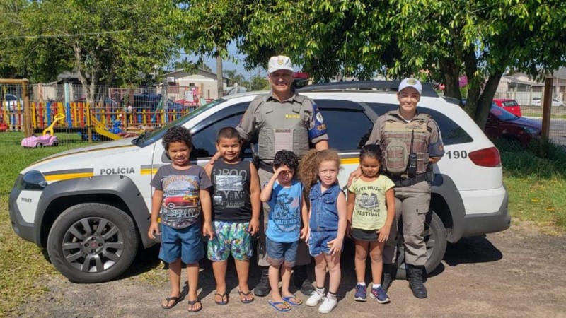 Policiais militares com grupo de alunos junto à viatura