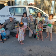 policiais militares ao lado da viatura com as crianças que receberam seus presentes de natal 