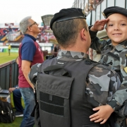 A foto mostra uma criança fardada no colo do pai policial