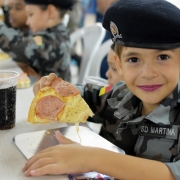  A imagem mostra uma menia  fardada comendo pizza