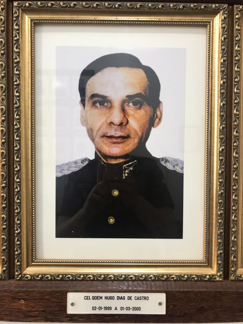 Quadro com moldura com a foto do Coronel RR Hugo Dias de Castro ao centro. n moldura abaixo o período de oficio como Chefe do Estado-Maior da Brigada Militar