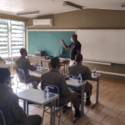 Foto dentro de uma sala de aula com alunos-soldados fardados sentados em mesas escolares