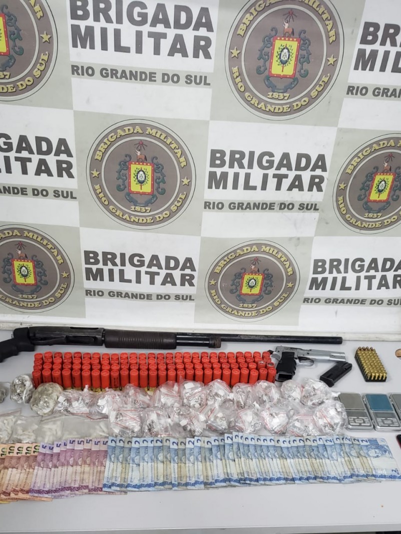 A foto mostra todos os itens apreendidos em cima de uma mesa, como as armas, diversas munições, pacotes de drogas e notas de dinheiro