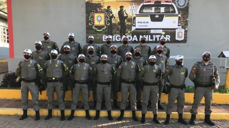 Alunos soldados do Polo de ensino Rio Pardo equipados, juntamente com o instrutor 1º Sargento Dias em frente a um banner da Brigada Militar.