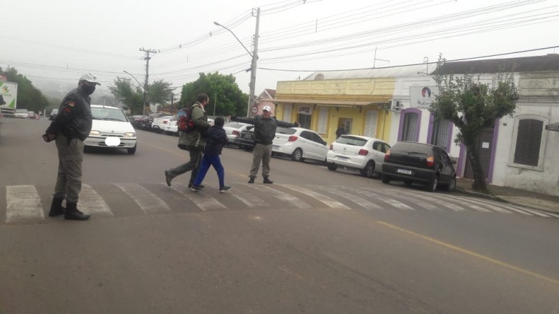 Dois policiais militares parando o trânsito para que pedestres atravessem em segurança a faixa de segurança