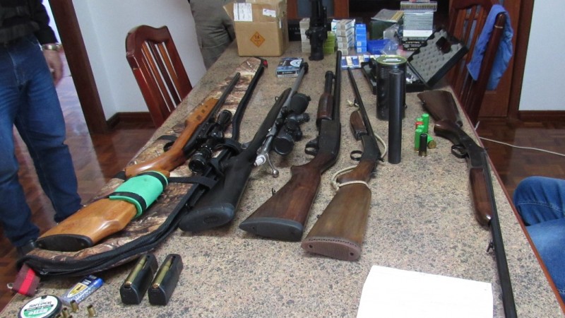 Foto das armas e outros itens apreendidos em cima de uma mesa