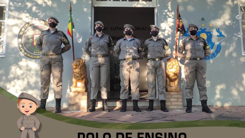 Cinco alunas-soldados perfiladas e ao fundo o quartel da escola de formação.