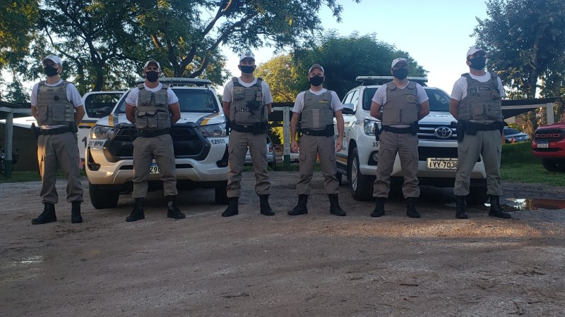 Policiais Militares perfilados a frente de duas viaturas.