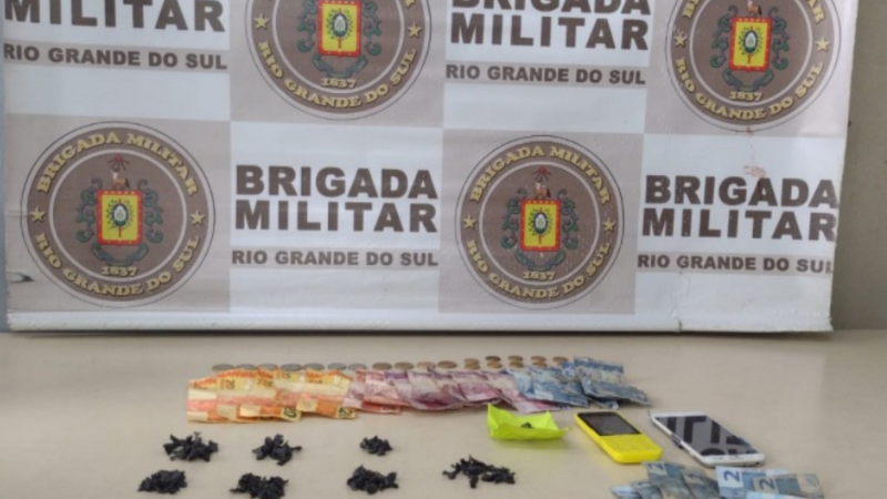 A imagem mostra um banner quadriculado nas cores branco e bege com o brasão e o nome "Brigada Militar - Rio Grande do Sul", apresentando mais a frente, o material apreendido. 