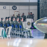 Imagem mostra, em primeiro plano, uma hélice de avião e, em segundo plano, os alunos-oficiais formandos sentados na cerimônia