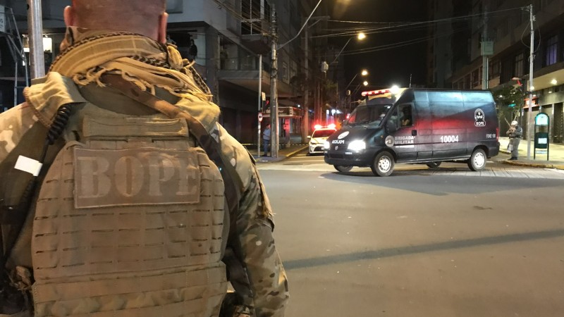 Imagem noturna mostra soldado do Bope de costas em primeiro plano e viatura fechando rua em segundo plano.