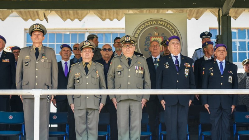 Cinco homens fardados em pé, parados lado a lado em posição de sentido. 