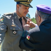 Homem de pé tendo uma medalha sendo colocada na gola de sua farda.