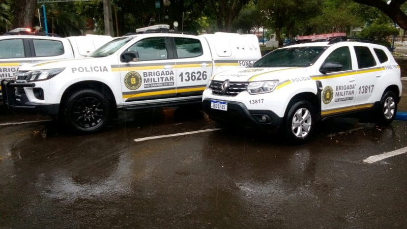 Três viaturas da BM estão estacionadas lado a lado sobre um chão molhado.