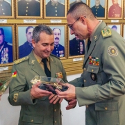 Dois militares estão de pé enquanto um deles entrega um presente ao outro