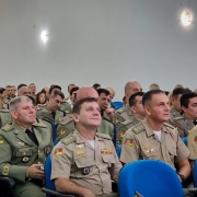 Grupo de militares está sentado em auditório assistindo a cerimônia