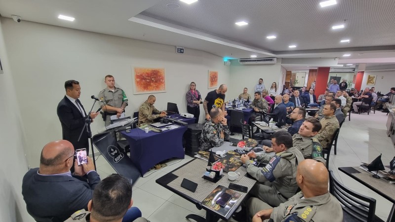 Um salão cheio de mesas onde um grande grupo de pessoas estão sentadas, na maioria militares.