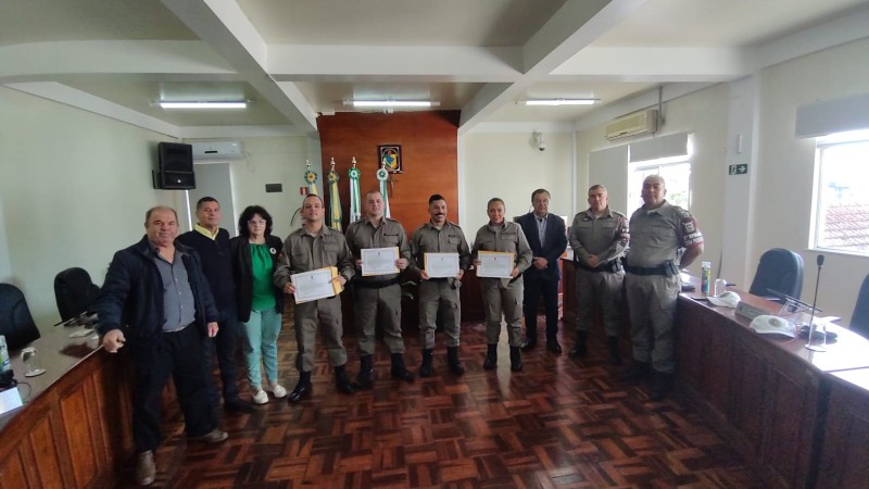 A fotografia mostra diversas pessoas, políticos e policiais militares. Os policiais militares estão com certificados em mãos, que receberam em homenagem ao seu trabalho realizado.