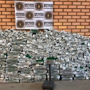 Tijolos de maconha estão empilhados em frente a uma parede de tijolos com um banner da BM