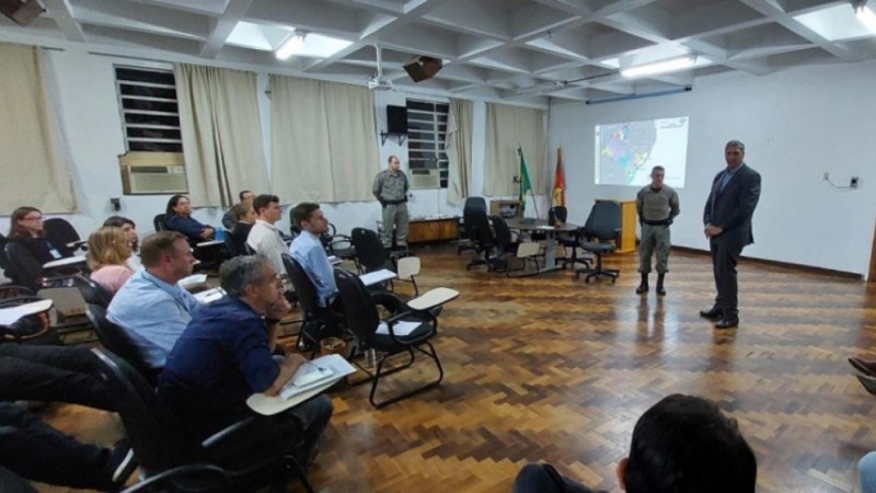 Imagem mostra uma sala com diversas pessoa sentadas. Na parte da frente, com datashow ligado, dois homens estão em pé