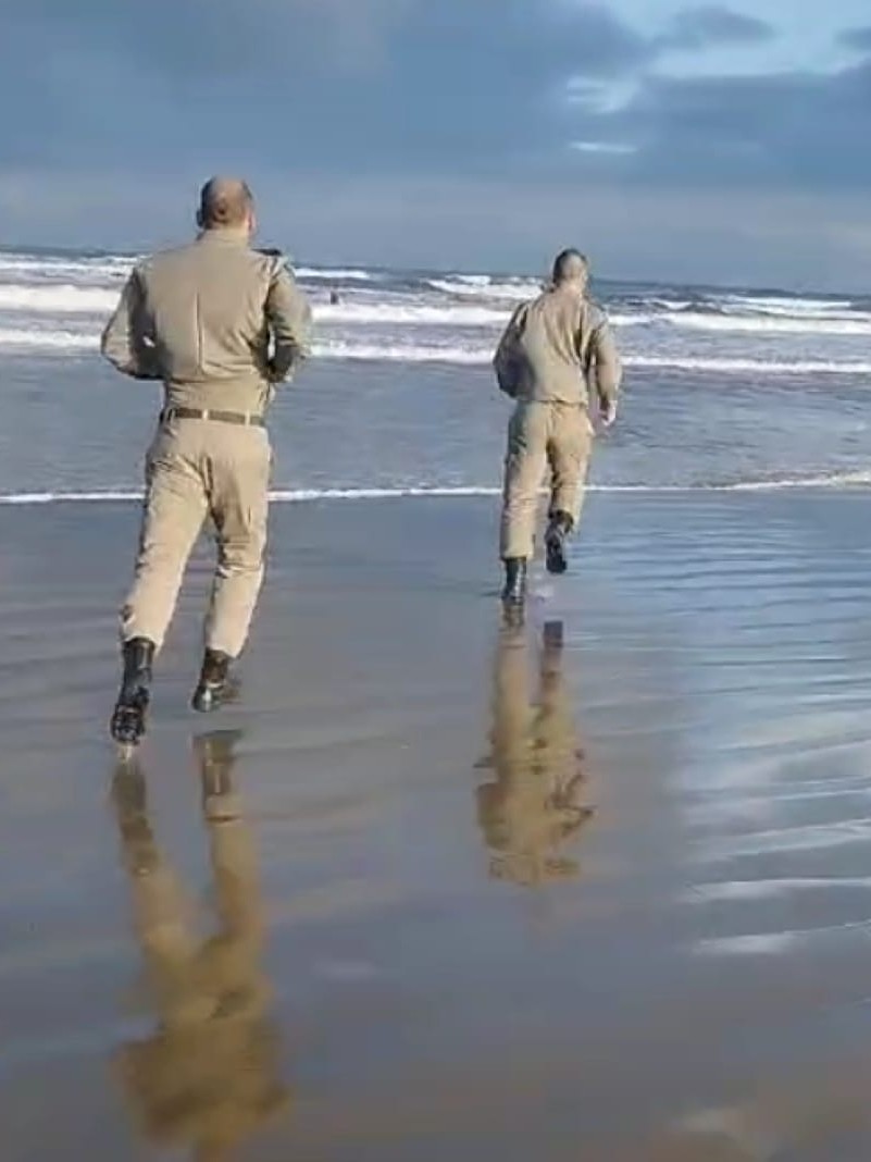 Policiais militares correm em direção ao mar para efetuar o salvamento de um homem que se afogava