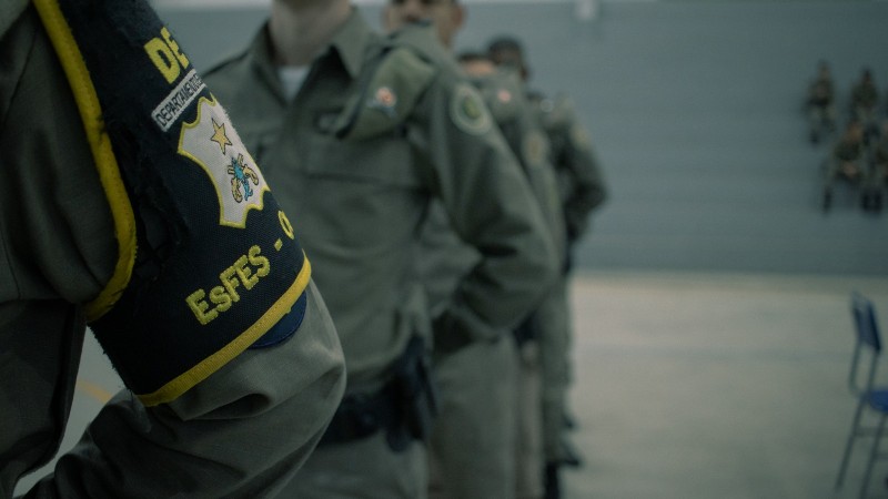 Foto com filtro aplicado mostra cinco policiais militares em forma, em posição de descanso
