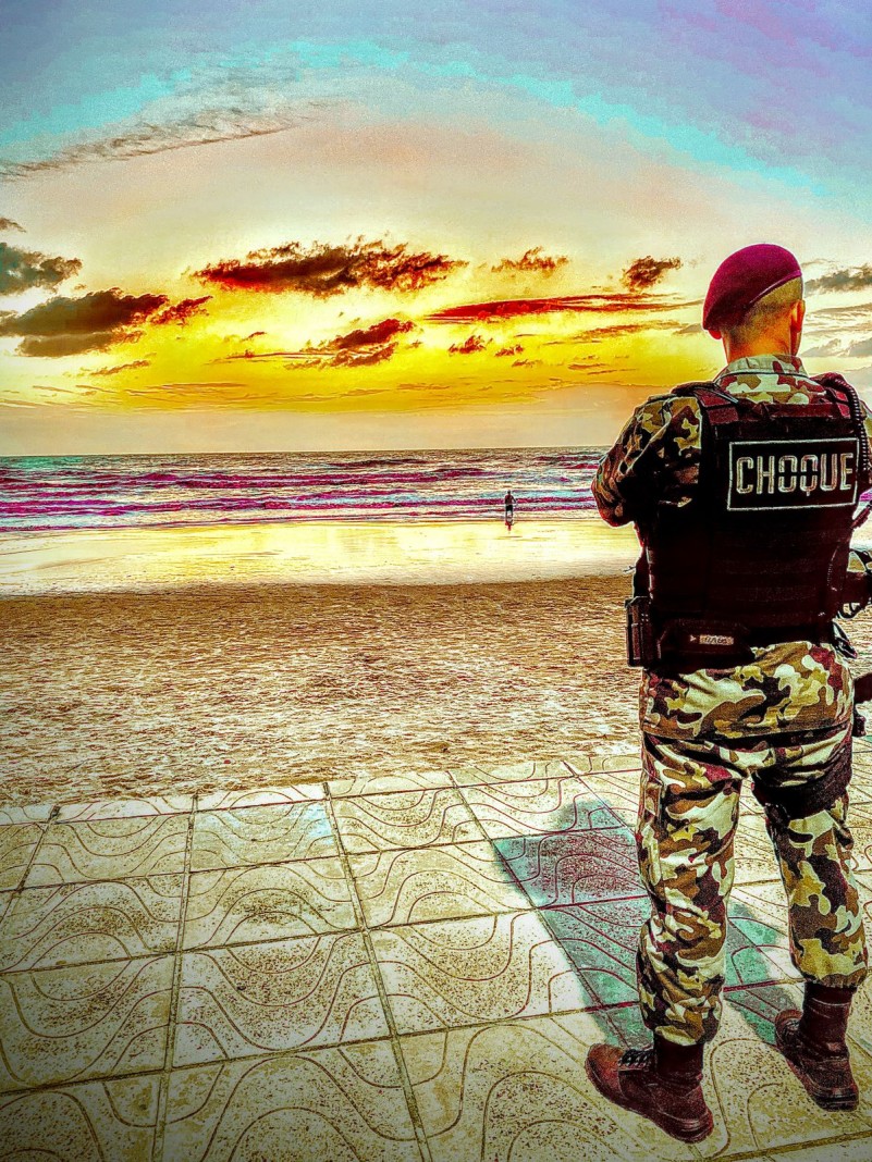 Foto mostra policial do Choque em pé em frente a uma praia, durante a Operação Golfinho.