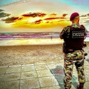 Foto mostra policial do Choque em pé em frente a uma praia, durante a Operação Golfinho. 