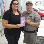 Na foto, uma policial militar realiza a entrega de um folder educativo, sobre proteção das mulheres, para uma funcionária do comércio.