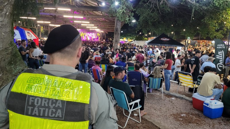 Um policial militar com colete reflexivo da BM em frente ao público.