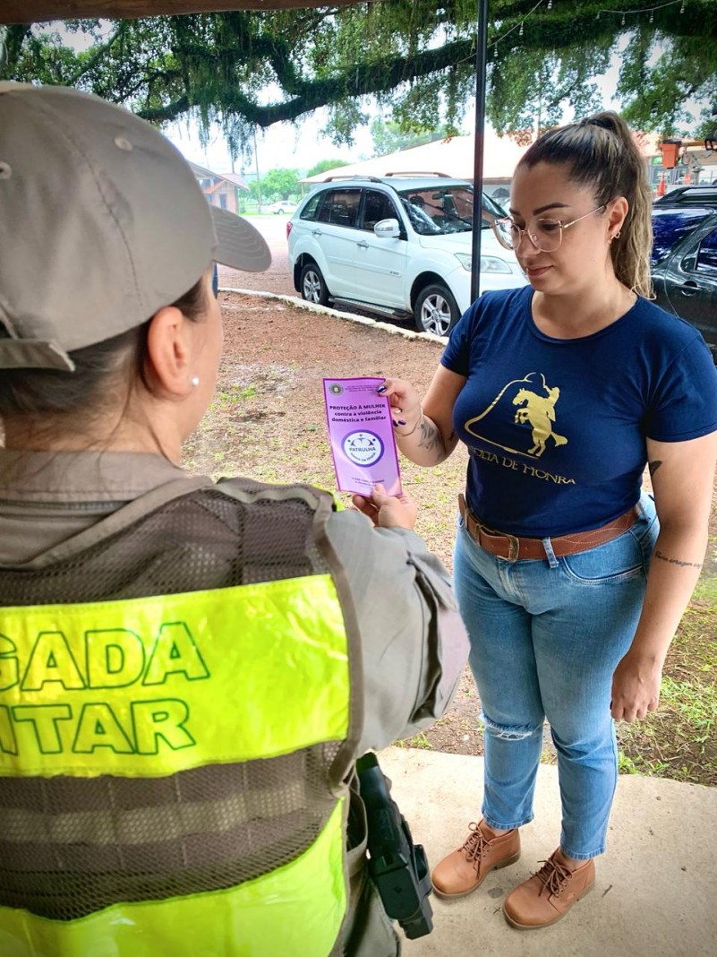Uma policial militar entregando um panfleto a uma mulher.