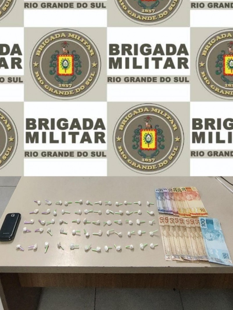 Ao fundo, banner da Brigada Militar, e sobre a mesa, 60 pinos de cocaína e 579 reais