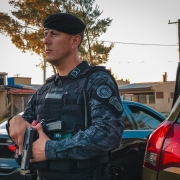 Policial militar das Patrulhas Especiais realizando segurança durante abordagem. Ele segura uma pistola na posição sul, visando a segurança dos policiais militares