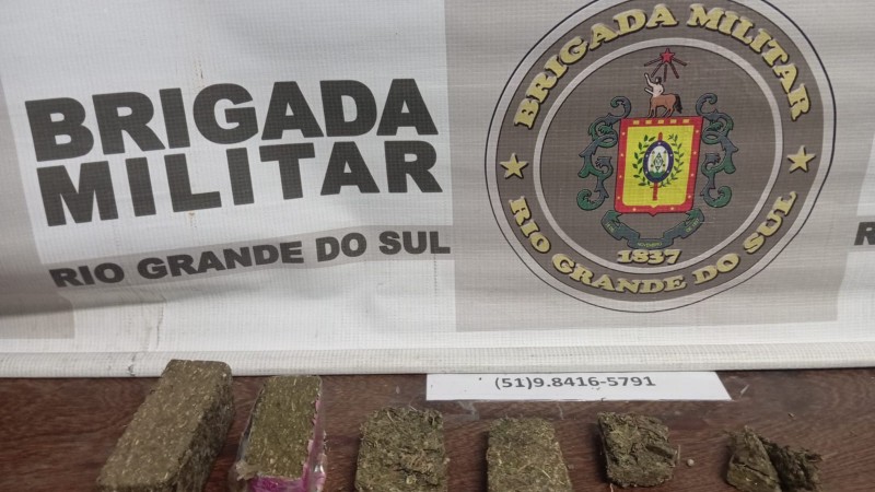 porções de droga encima de uma mesa em frente ao banner da BM