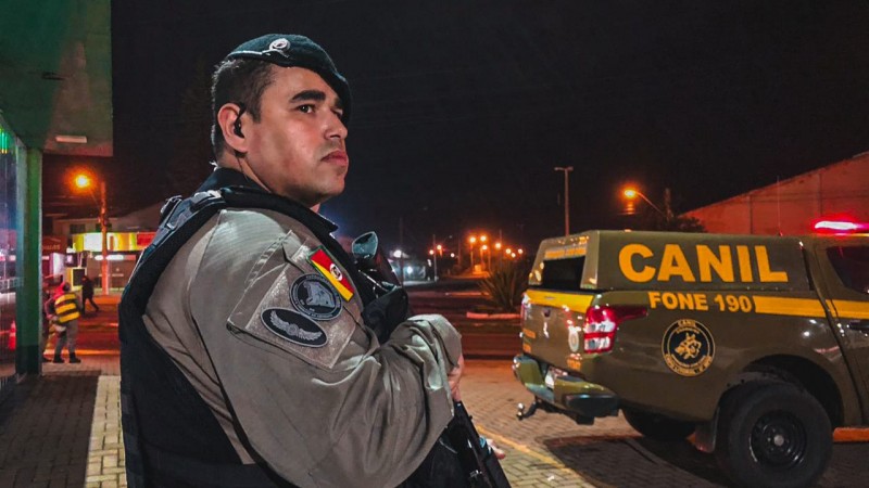 Policial militar da Força Tática do 8ºBPM fazendo policiamento, ao fundo, uma viatura do Canil