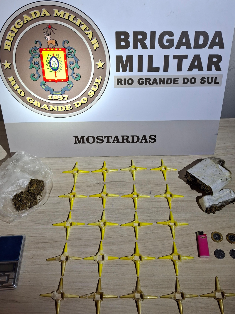 Ao fundo um banner da Brigada Militar e em cima de uma mesa as apreensões: 84 pinos de cocaína, 240 gramas de maconha e uma balança de precisão