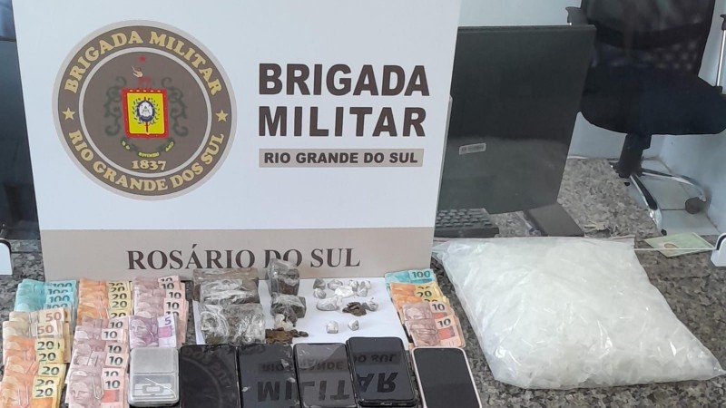 Em cima da mesa, encontram-se diversos materiais apreendidos: dinheiro, celulares, drogas e embalagens para comercializar as drogas.