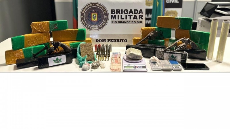 Diversos tijolos de entorpecentes, muni&ccedil;&otilde;es e armas apreendidas, juntamente com notas de dinheiro, celulares, balan&ccedil;a de precis&atilde;o.