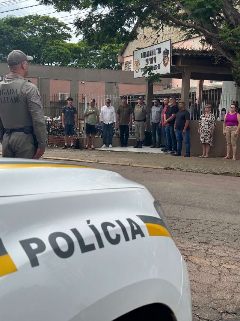 Na imagem possui um policial militar, parte de uma viatura da BM e personalidades civis que participaram da solenidade.