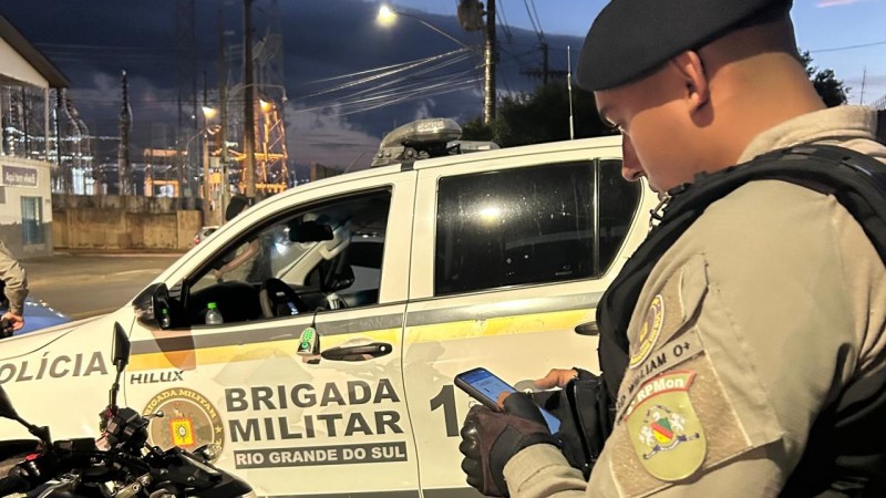 Na foto contén um policial, uma viatura e uma motocicleta