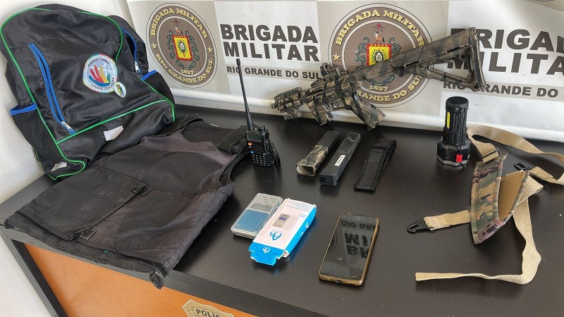 Na foto contém um colete balístico, marca CBC, com capa, balança de precisão, lanterna tática e um rádio comunicador, na frequência da Brigada Militar.