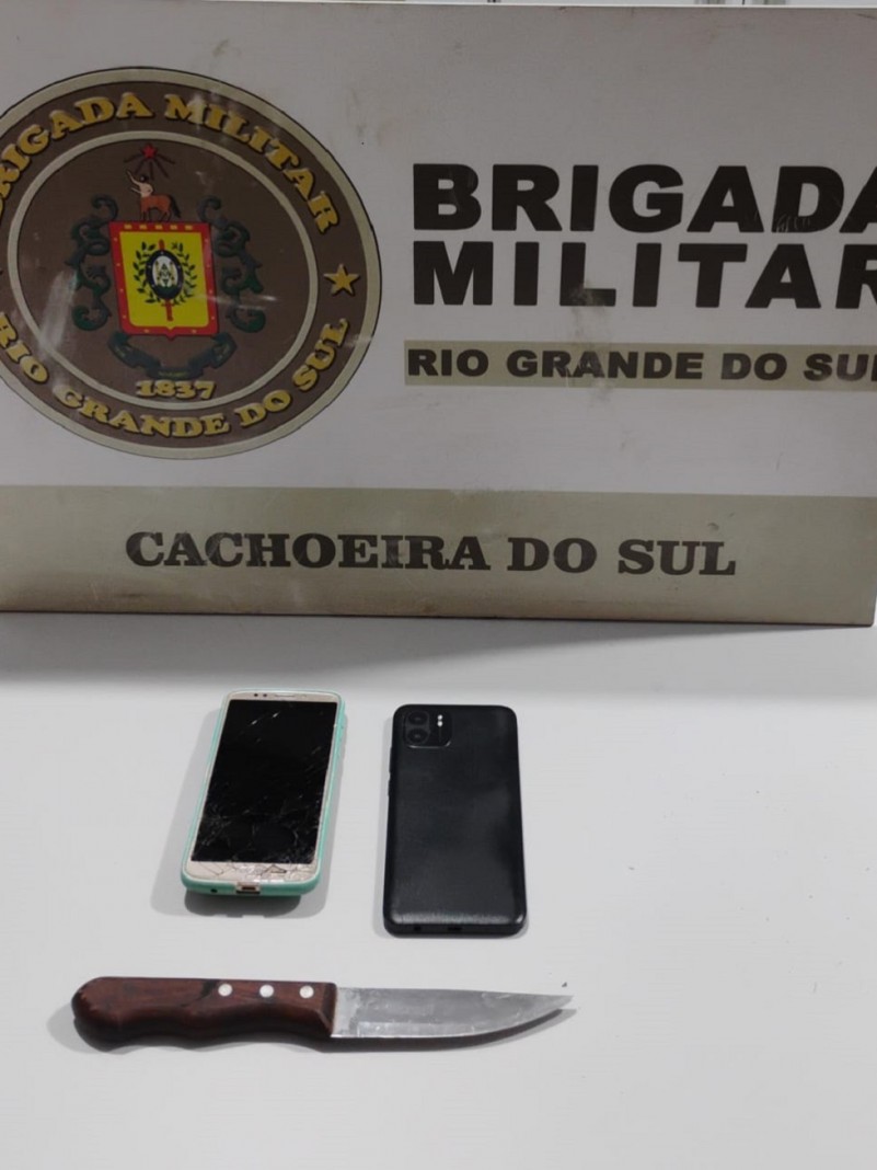 Sobre uma mesa de cor branca encontram-se dois aparelhos celulares e uma faca com cabo de madeira, aprendidos em decorr&ecirc;ncia de objetos de furtados.