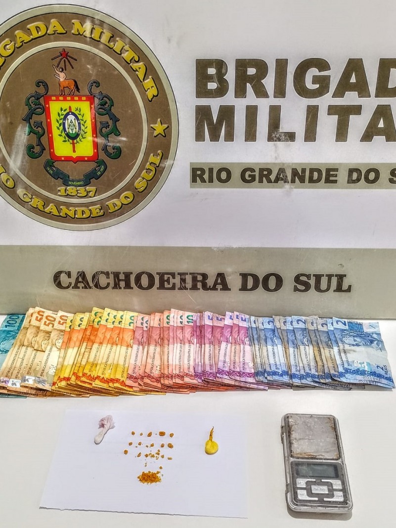 Sobre uma mesa est&atilde;o drogas fracionadas, uma balan&ccedil;a de precis&atilde;o e R$1088,00 em esp&eacute;cie.