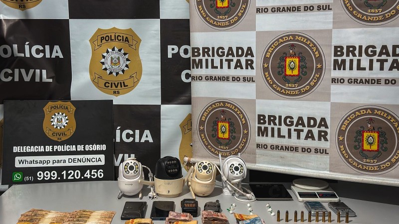 Ao fundo , banner da BM e PC, em cima de uma mesa, drogas, dinheiro, câmeras de videomonitoramento, faca, balança de precisão