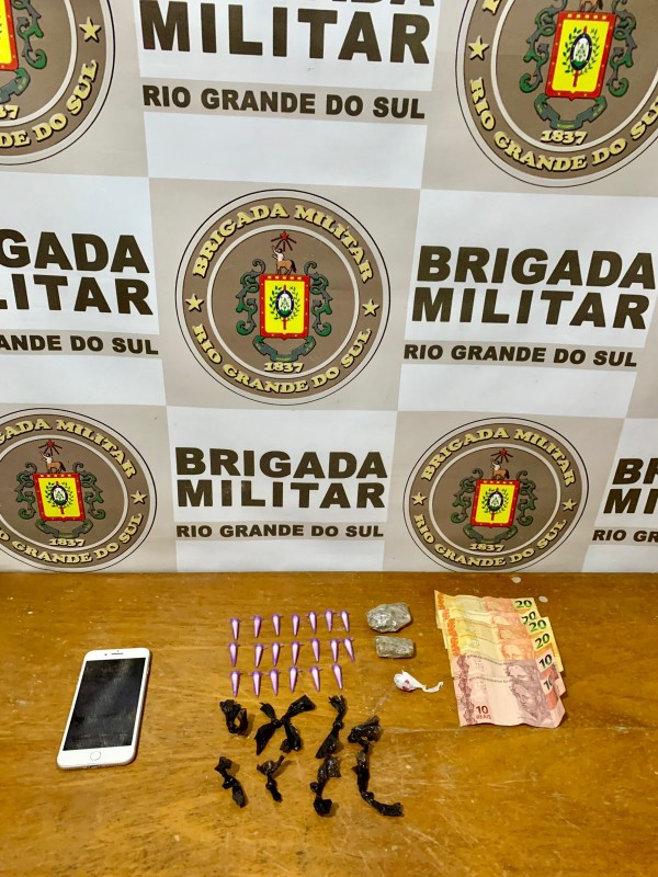 maconha, cocaína e crack dispostos em uma mesa e ao fundo banner da Brigada Militar