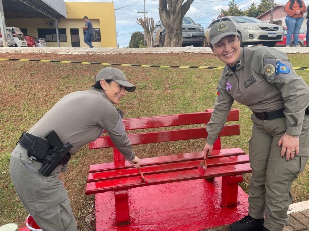 Dupla de policiais militares femininas pintam um banco vermelho 