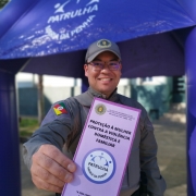 Policial Militar masculino mostra sorrindo ao folder da Patrulha Maria da Penha 