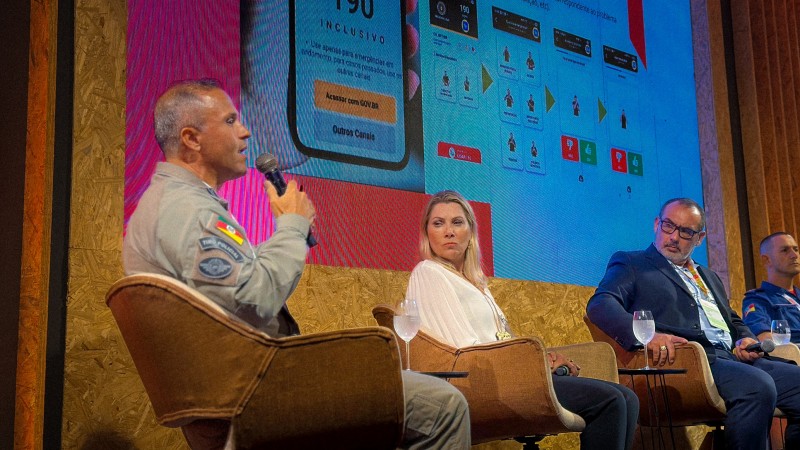Foto mostra o major major Arthur no palco, com o microfone na m&atilde;o, junto aos outros participantes do painel