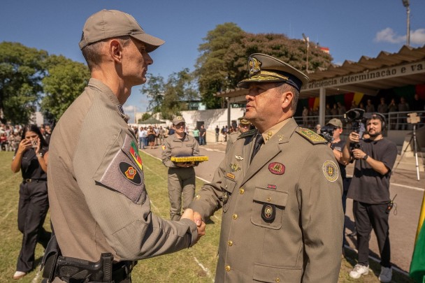 O soldado PM recebe o aperto de mão do Comandante-Geral. Em volta há fotógrafos registrando o momento.  